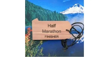 A wooden 'Half Marathon FINISHER' medal hangs against a backdrop of a snow-capped mountain and pine forest.