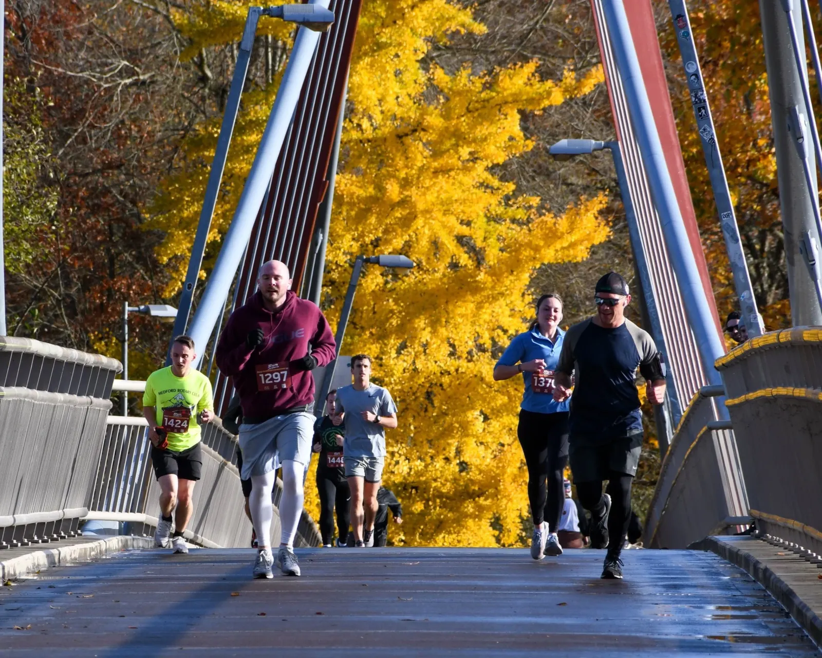 Runners crossing a bridge with vibrant yellow fall foliage in the background.