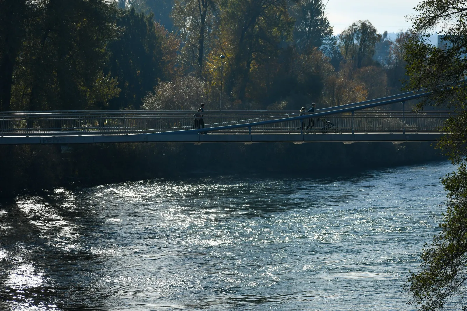 People walking across a bridge over a river on a sunny day.