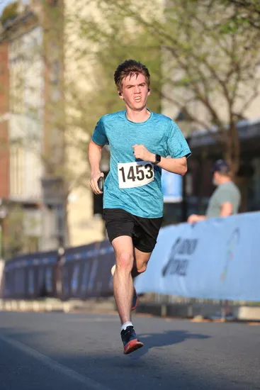 A young male runner with bib number 1453 runs on a road during a race.