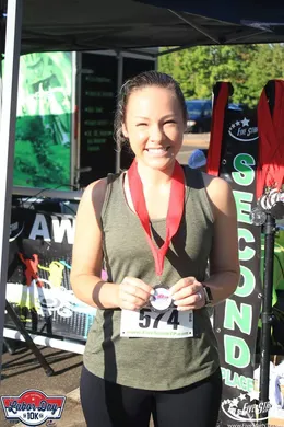 A smiling woman wearing a race medal and bib number 574.