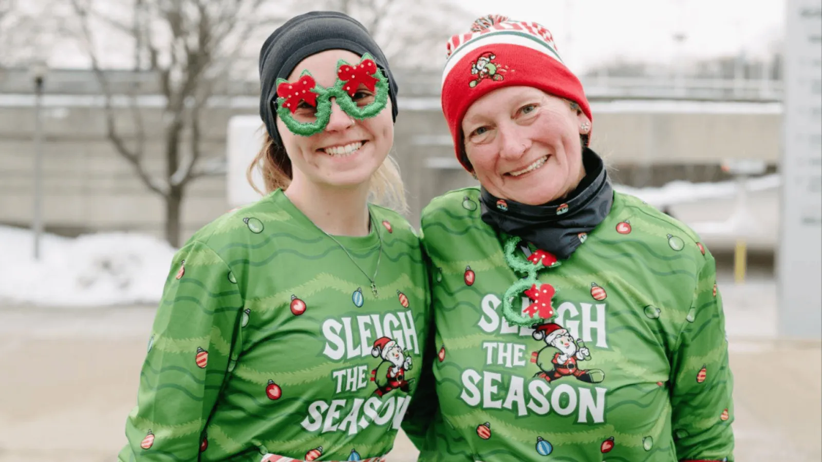 Two women smiling at the camera, wearing festive Christmas-themed running shirts and accessories.