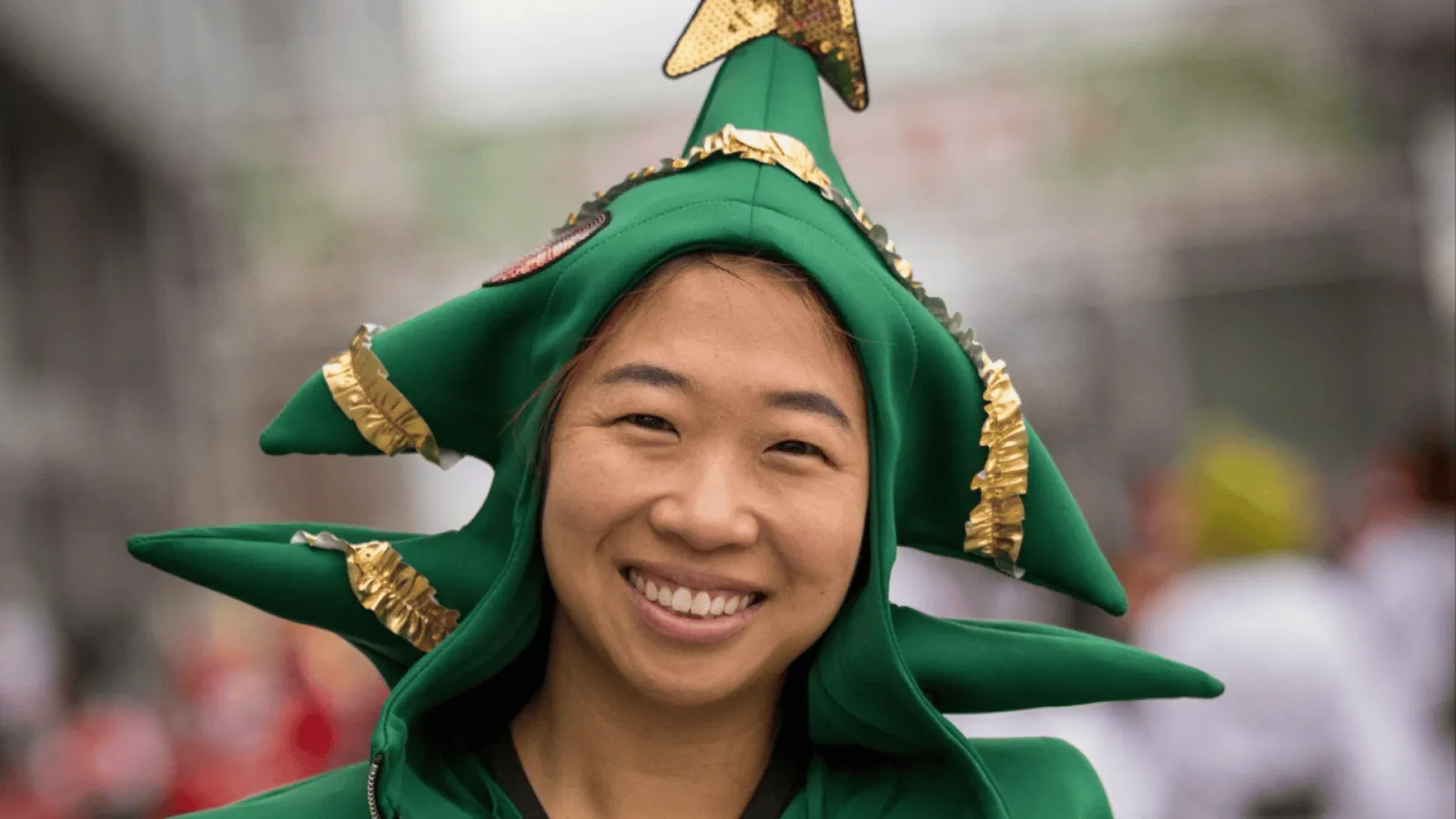 A smiling runner wearing a green Christmas tree costume and hat at a race.
