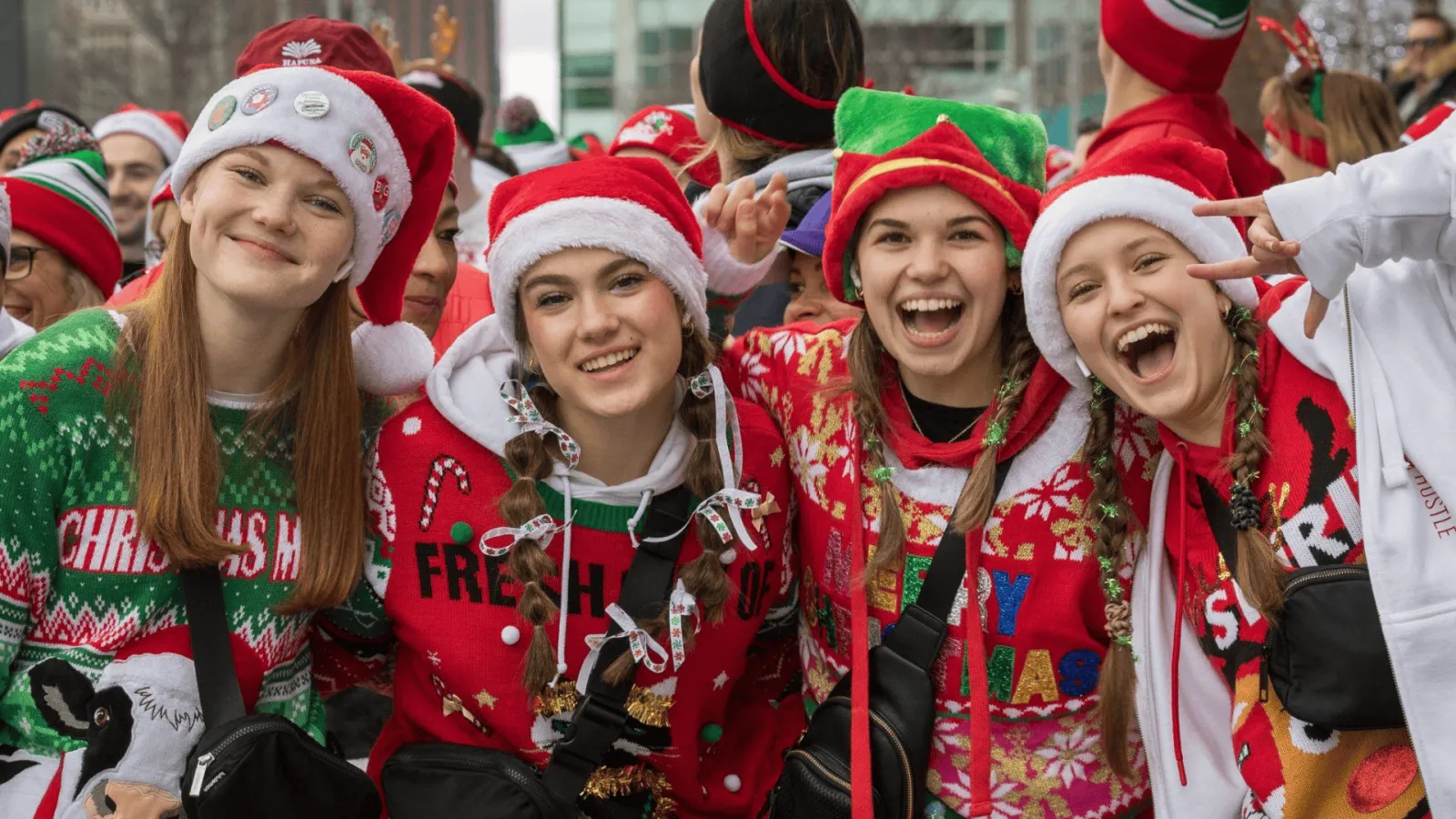 A group of young women in festive Christmas sweaters and Santa hats smile and laugh, posing for a photo at a race event.