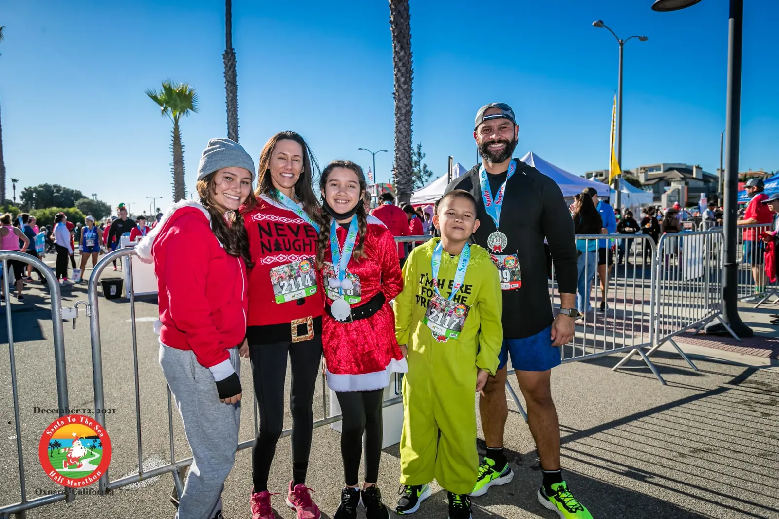 A group of five people, including children, smiling and posing for a photo after a race, all wearing medals.