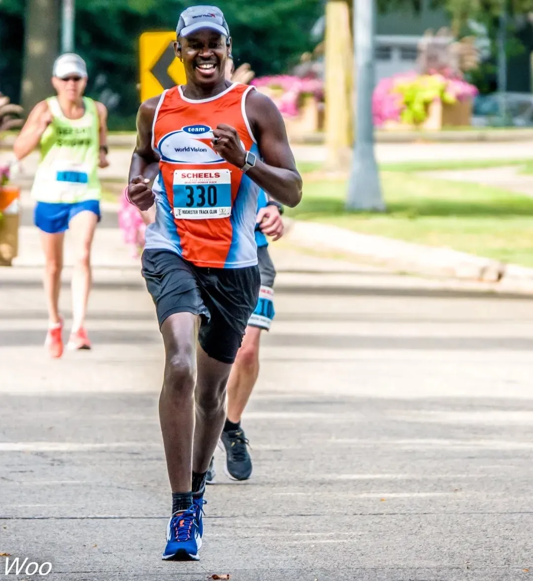 A male runner smiles as he runs down a road during a race, wearing a bib number 330.