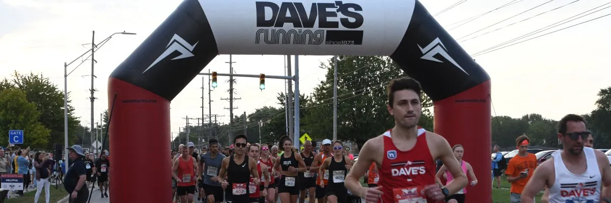 Runners starting a race under a large inflatable arch with 'Dave's Running' logo.