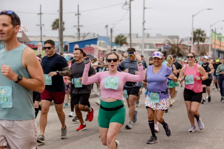 A group of runners participating in a race, with one woman in the foreground raising her arms in excitement.