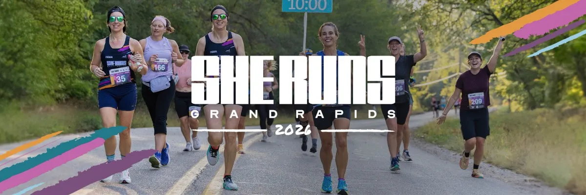 A group of women running a race, with the 'She Runs Grand Rapids' logo prominently displayed.