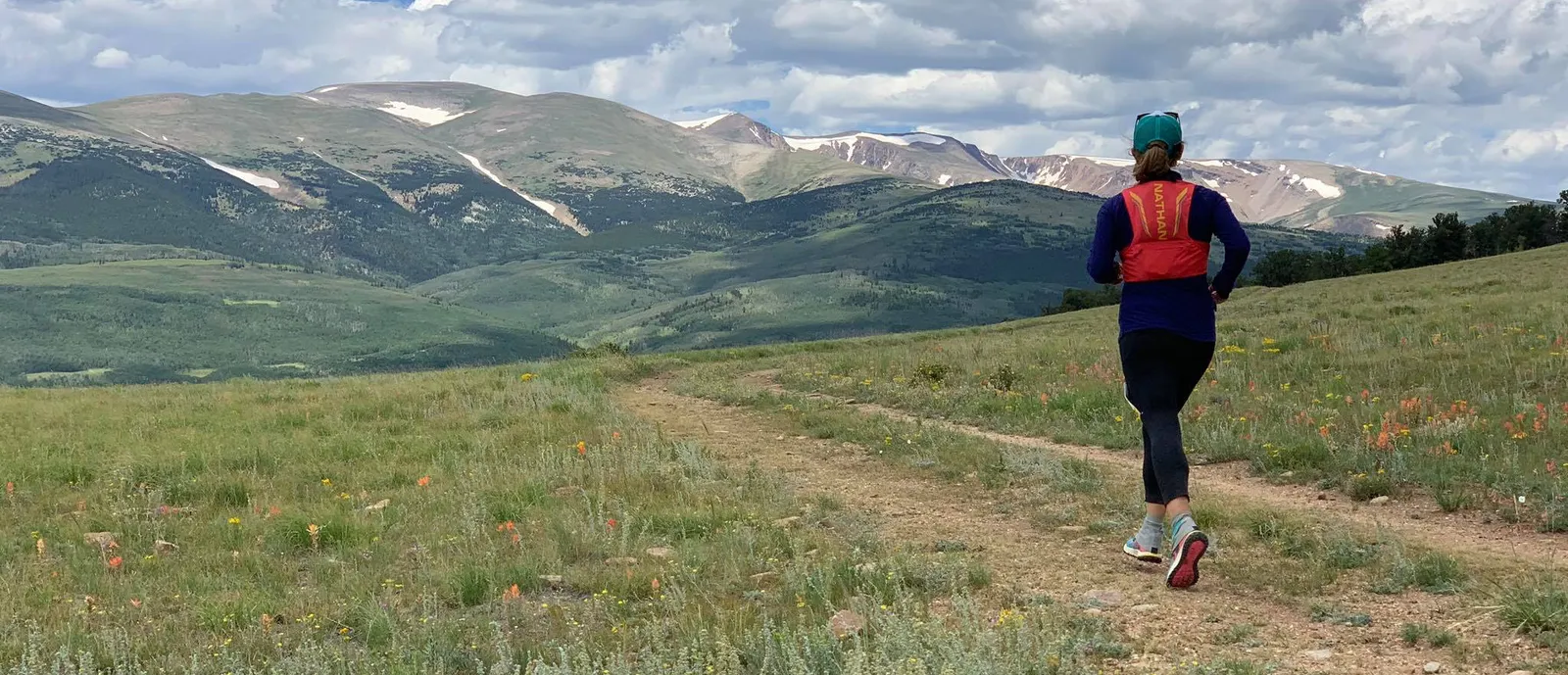 A runner on a trail with a scenic mountain backdrop.