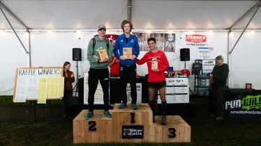Three male runners stand on a podium, holding awards, after finishing the Silver Falls Trail Half Marathon.