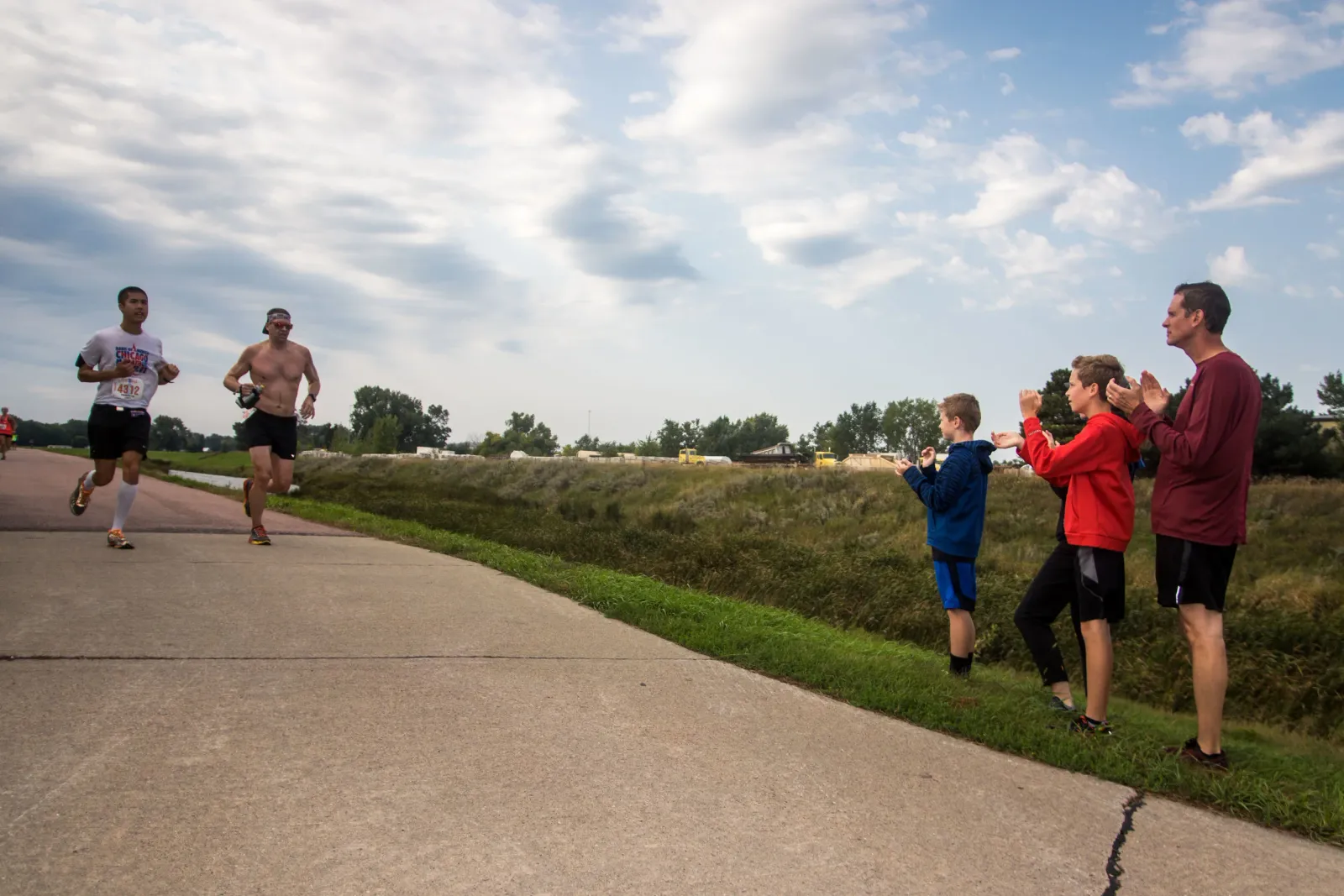 Runners on a paved path with spectators cheering from the side of the path.