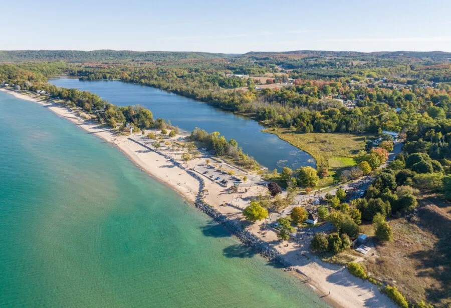 Aerial view of a race course along a sandy beach and a lake, with colorful autumn trees in the background.