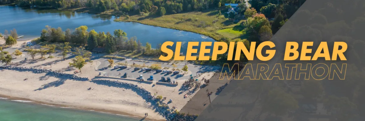 Aerial view of Sleeping Bear Marathon course with a lake, beach, and trees, featuring the race name in large yellow text.