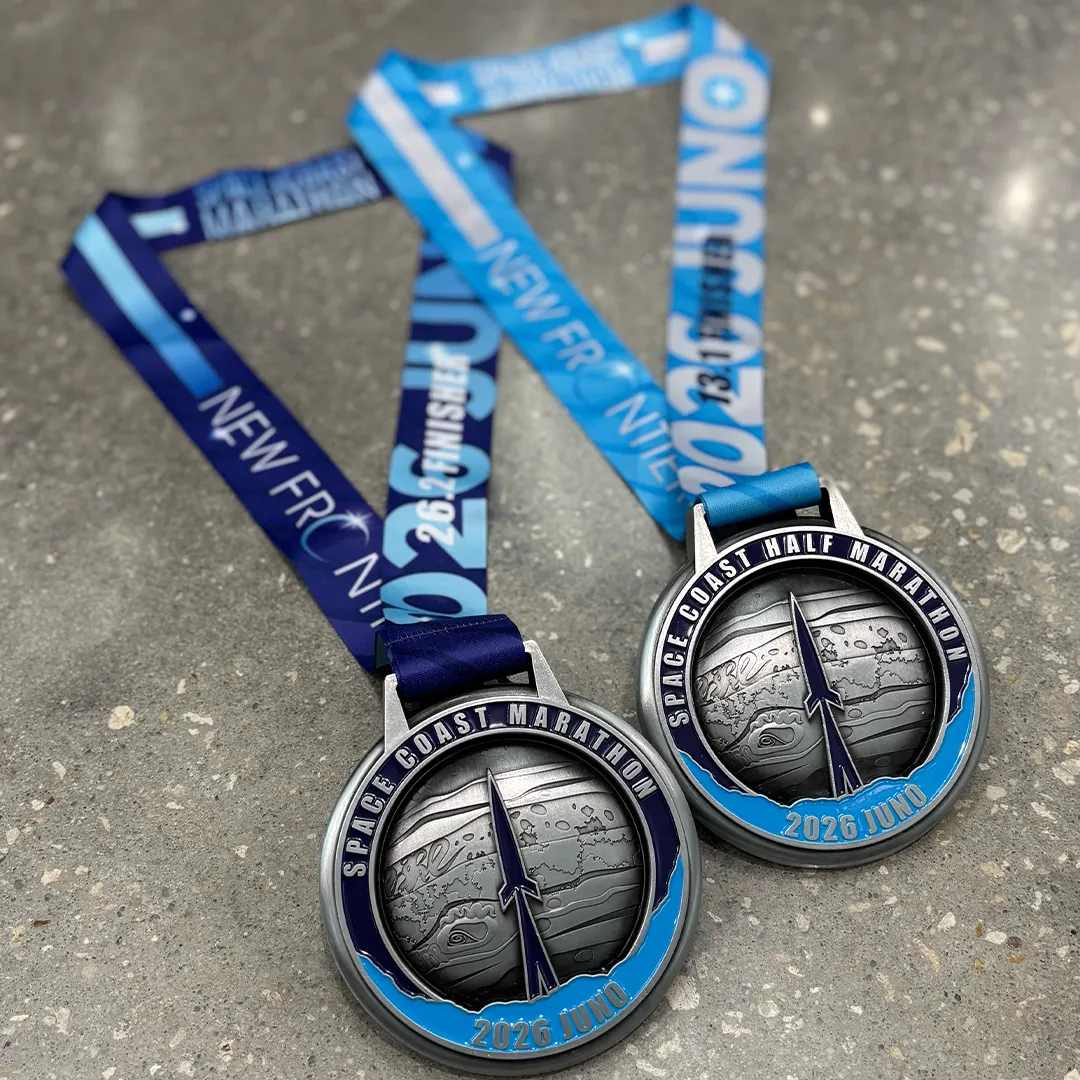 Two Space Coast Marathon and Half Marathon medals with blue ribbons, displayed on a grey surface.