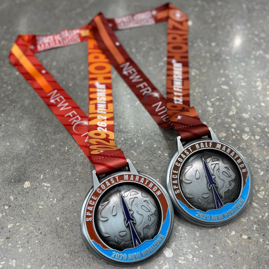 Two race medals for the Space Coast Marathon and Half Marathon, featuring designs related to space exploration and the year 2029.