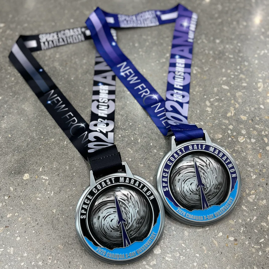 Two race medals for the Space Coast Marathon and Half Marathon, featuring a rocket and celestial imagery.
