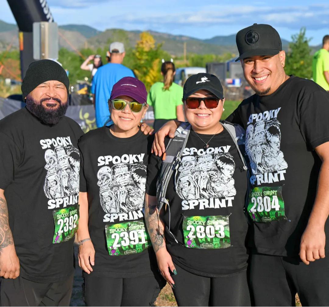 Four smiling participants wearing matching 'Spooky Sprint' t-shirts pose for a photo at the start line of a race.