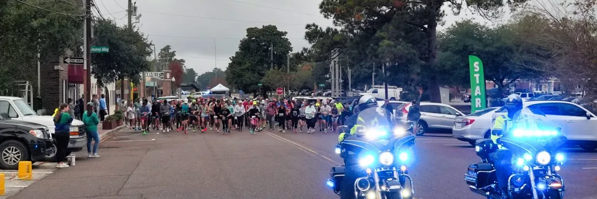 A large group of runners at the start line of a race, with police motorcycles in the foreground.