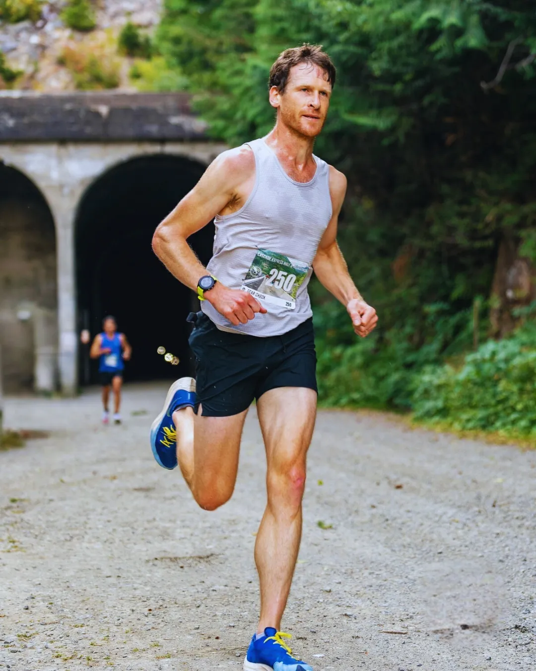 A male runner exits a tunnel on a gravel path, wearing a bib number 250.