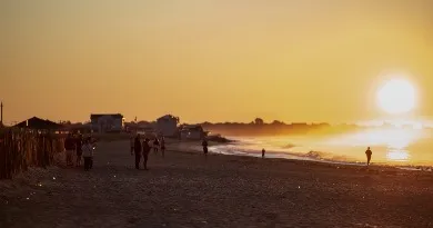 Sunrise over the ocean with people walking on the beach.