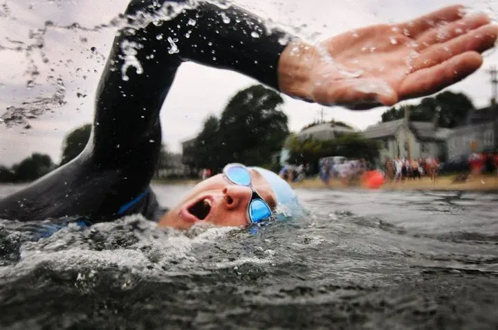 Swimmer in goggles and cap during a race, with water splashing.