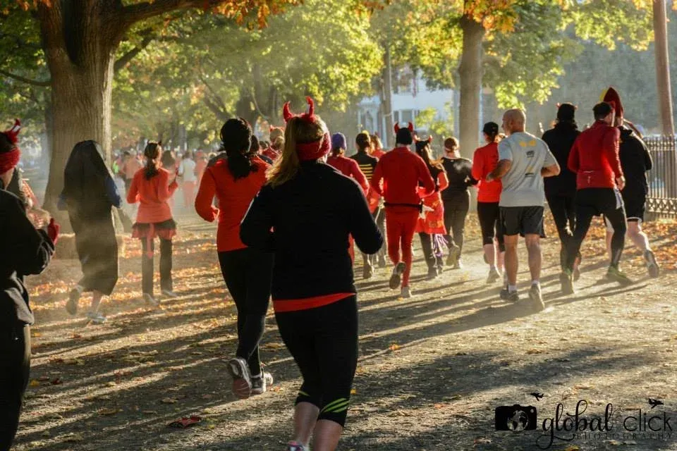 Runners with devil horns running on a tree-lined path during a race.