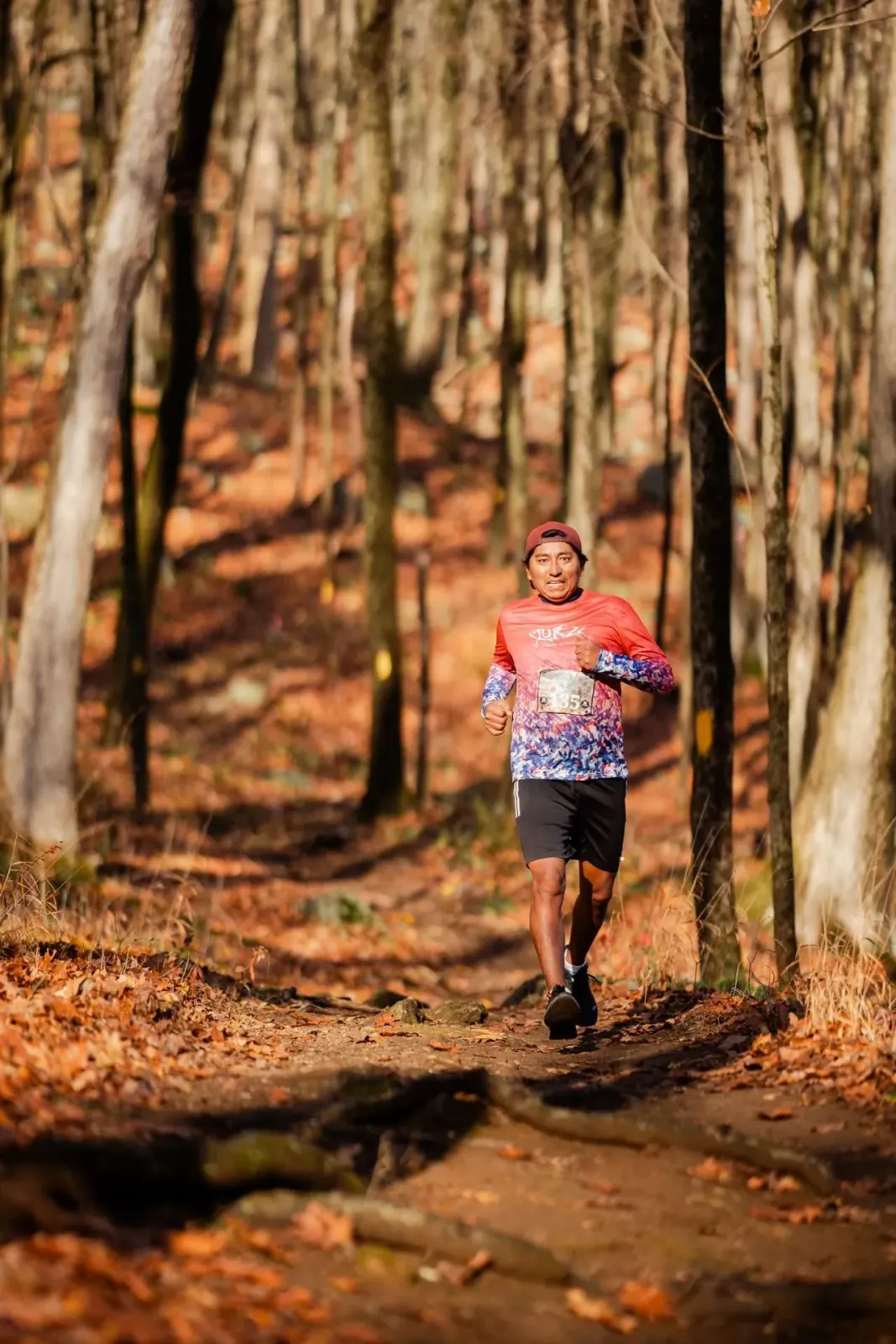 A male runner with a determined expression runs on a wooded trail during the Tarryville Half Marathon.