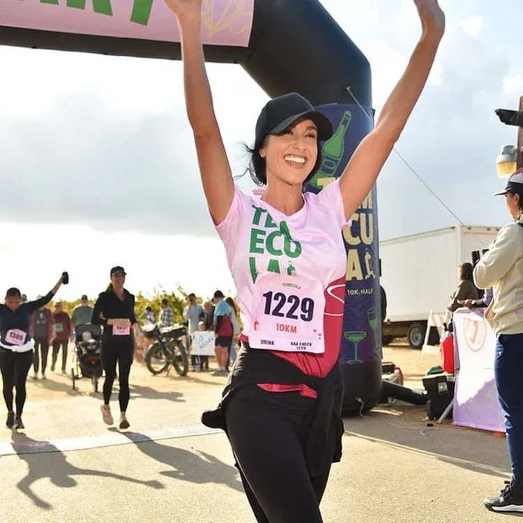A female runner with her arms raised in celebration crosses the finish line at the Wine Country Half Marathon.