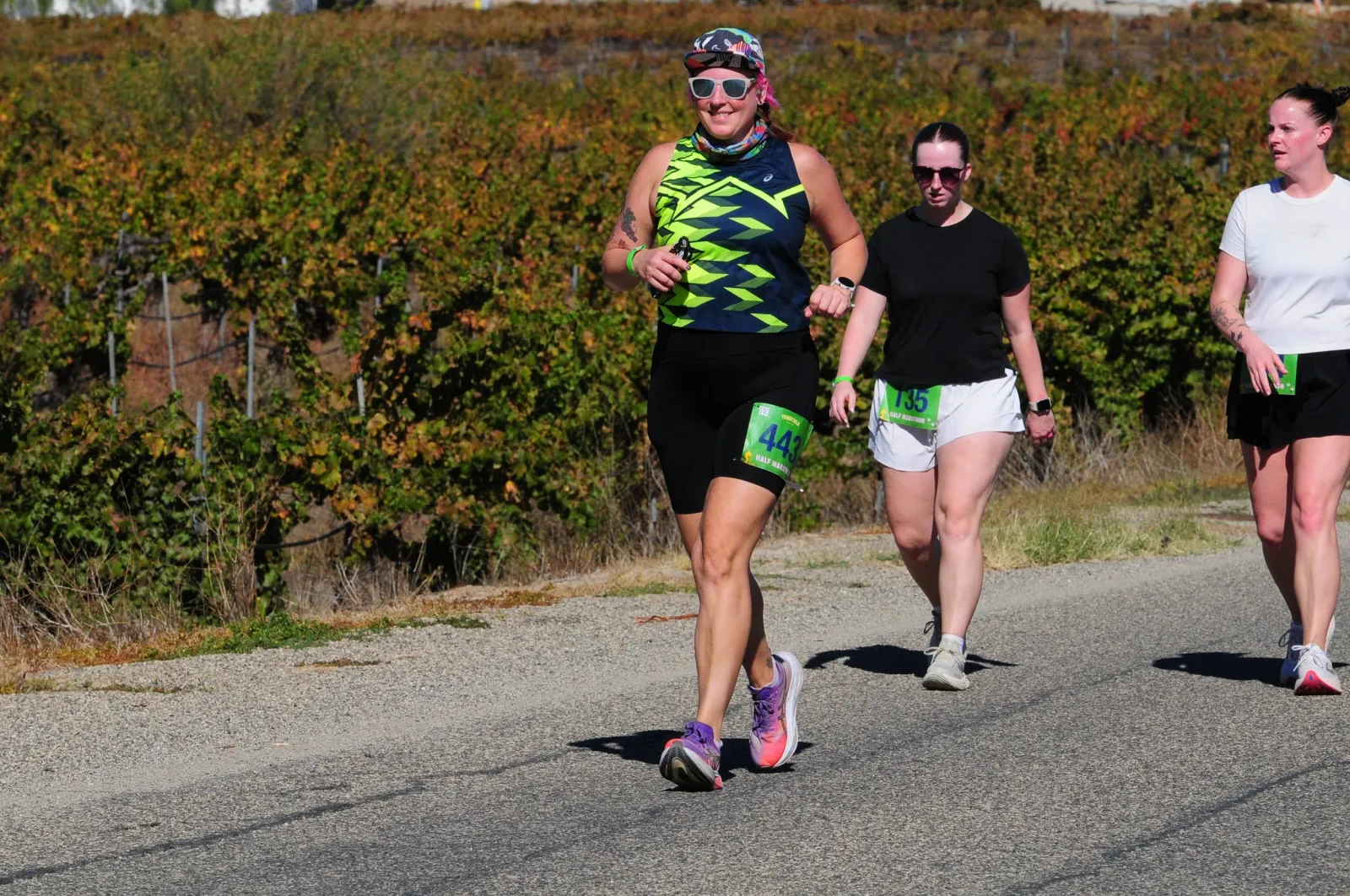 Runners on a road with vineyards in the background.