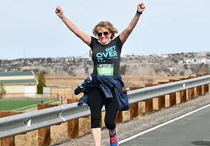 A female runner with arms raised in celebration as she crosses the finish line.