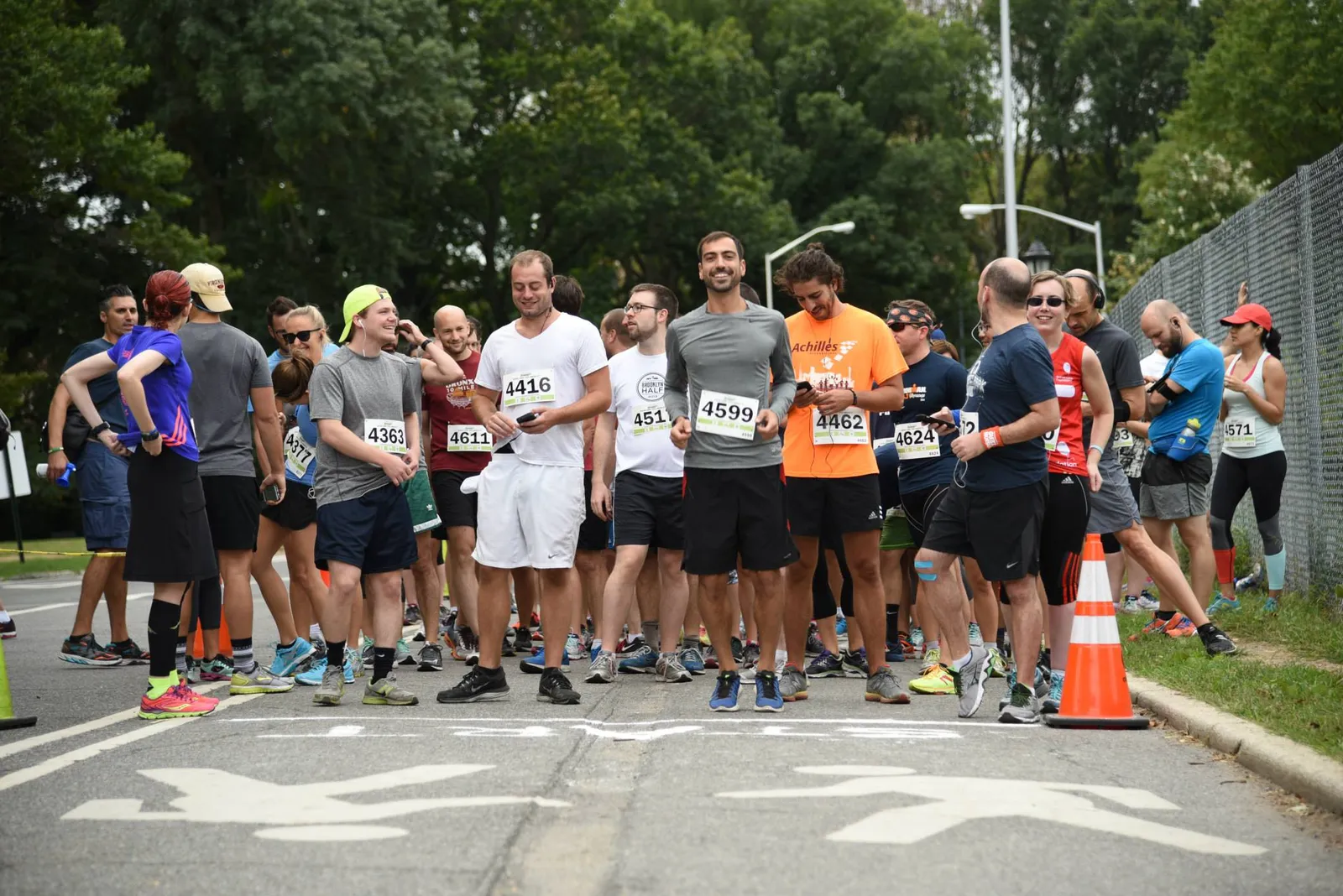 A group of runners stand at the start line of a race, looking towards the camera and checking their phones.