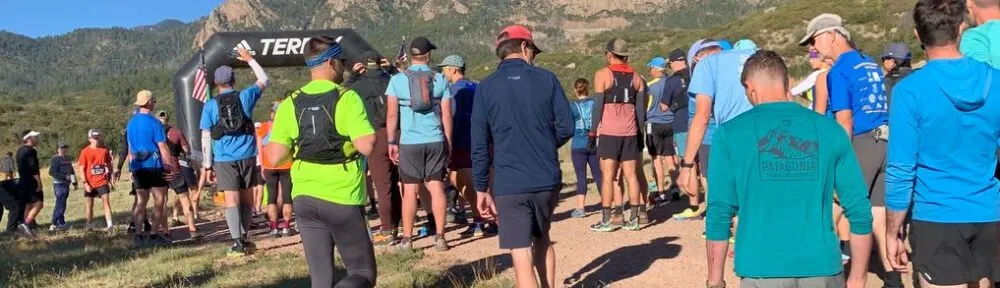 A group of runners gathered at the start line of a race, with an inflatable arch and mountains in the background.