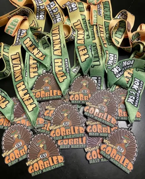 A pile of "The Gobbler" half marathon medals with green and yellow ribbons.