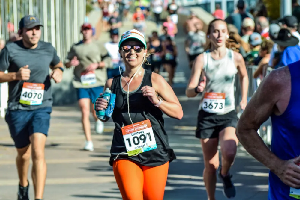 Runners participating in a half marathon, with a focus on a female runner in the foreground wearing orange leggings and a black tank top.