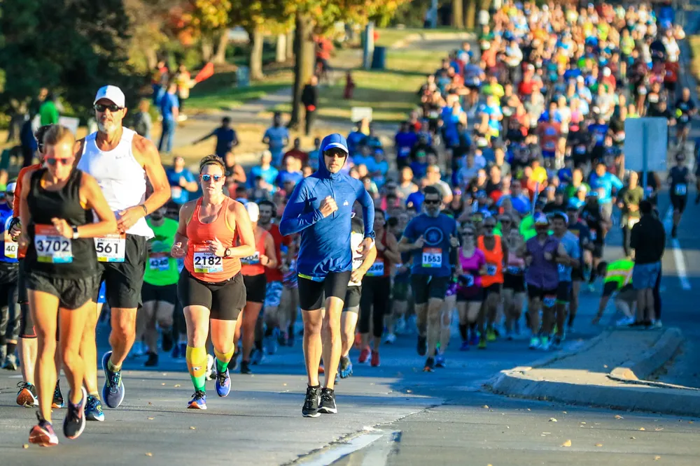 A large group of runners participating in a road race, with several individuals in the foreground in focus.