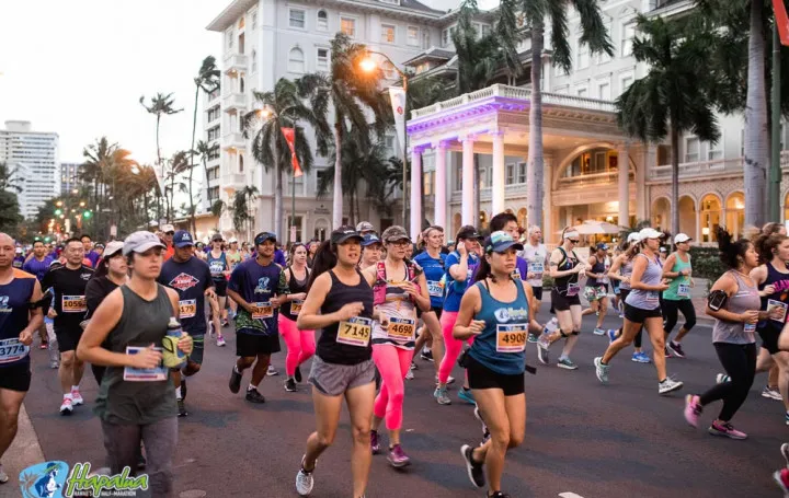 A group of runners participating in the Hapalua Hawaii Half Marathon, with palm trees and a historic building in the background.