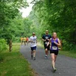 Runners on a paved path through a lush green forest.