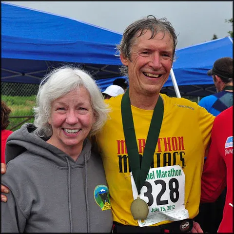 A smiling couple, one wearing a marathon medal and bib number 328, pose for a photo after a race.