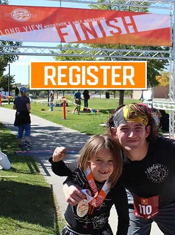 A young girl and an adult smile at the camera, both wearing race medals, with a finish line banner in the background.