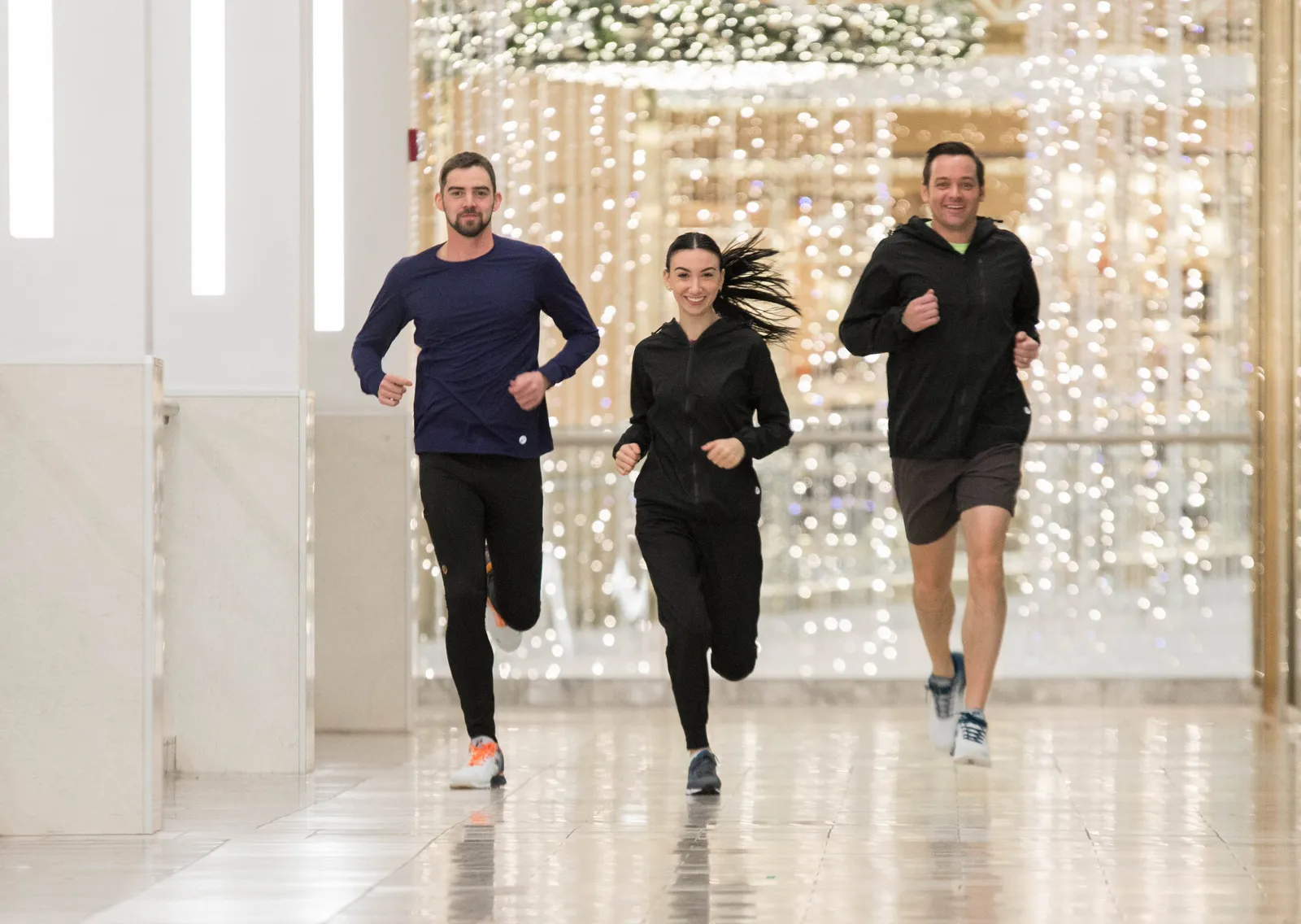 Three people running together indoors with a blurred background of festive lights.