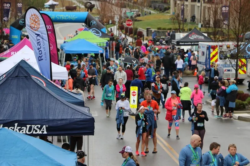 A crowd of runners and spectators gather near tents and an inflatable archway at the start or finish of a race.