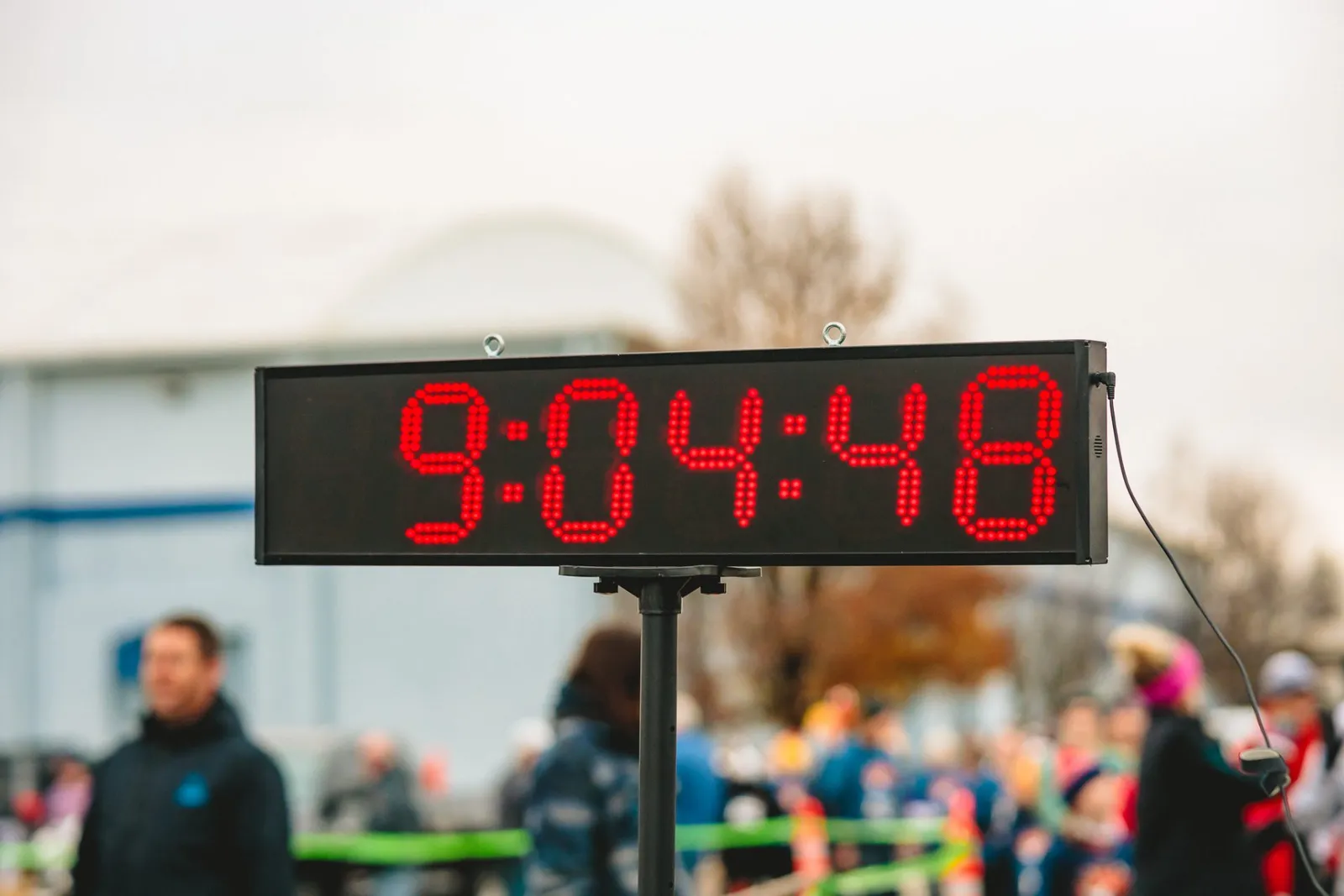 A digital race clock displaying 9:04:48 with blurred runners and spectators in the background.