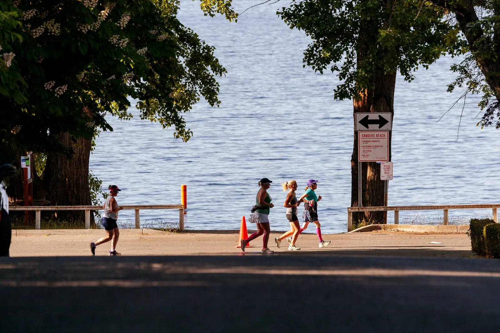 Runners on a paved path next to a large body of water.