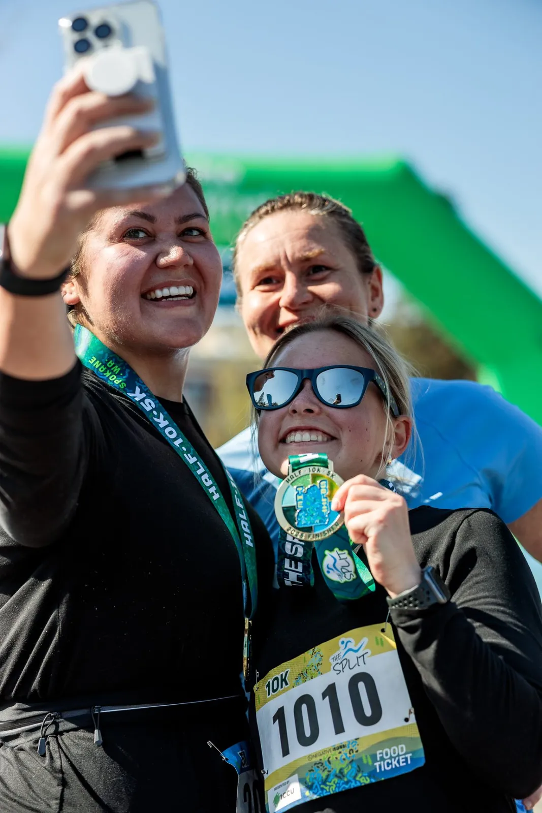 Three smiling runners pose for a selfie with their race medals after finishing a 10K race.