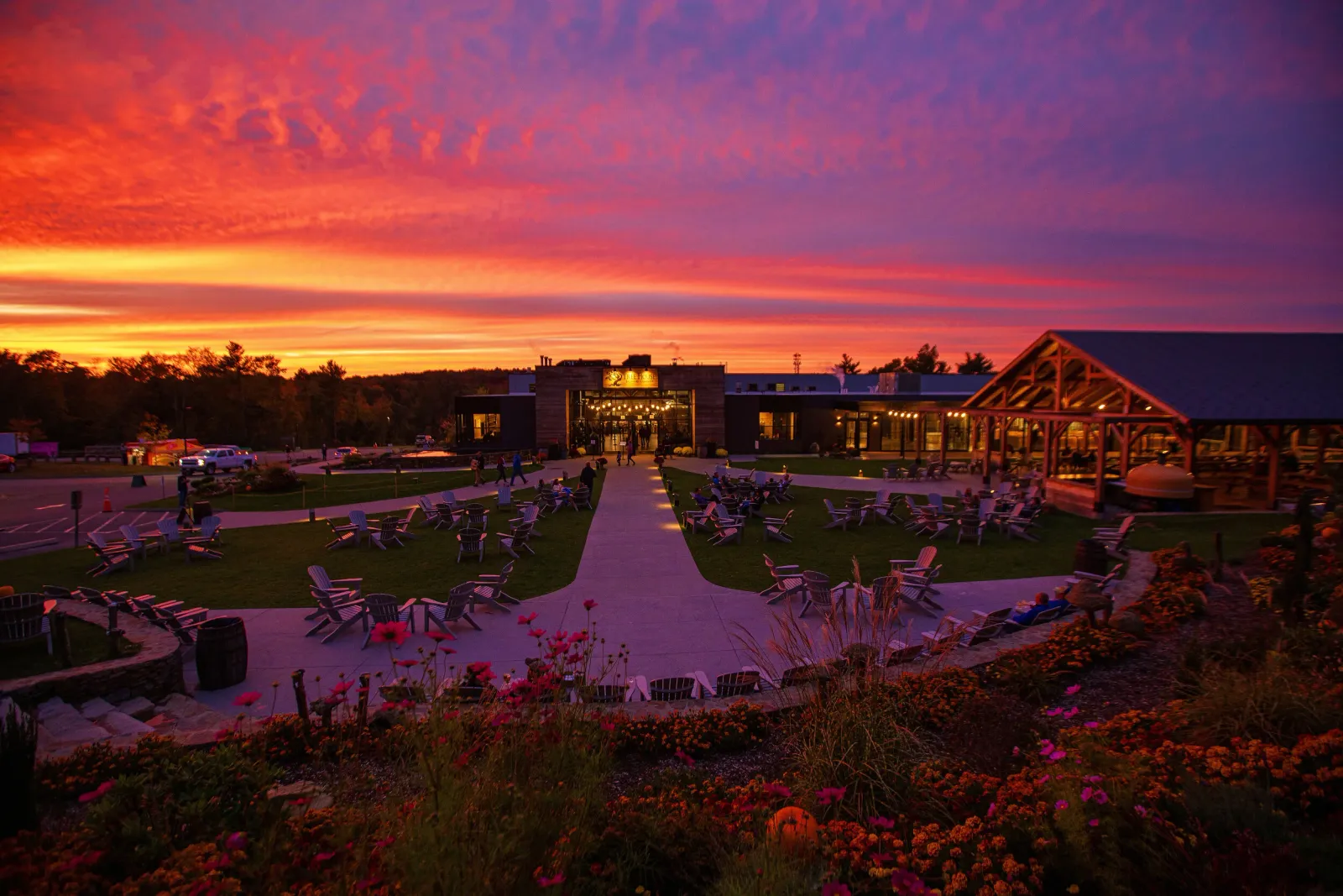 A vibrant sunset with orange, pink, and purple hues over a scenic venue with outdoor seating and buildings.