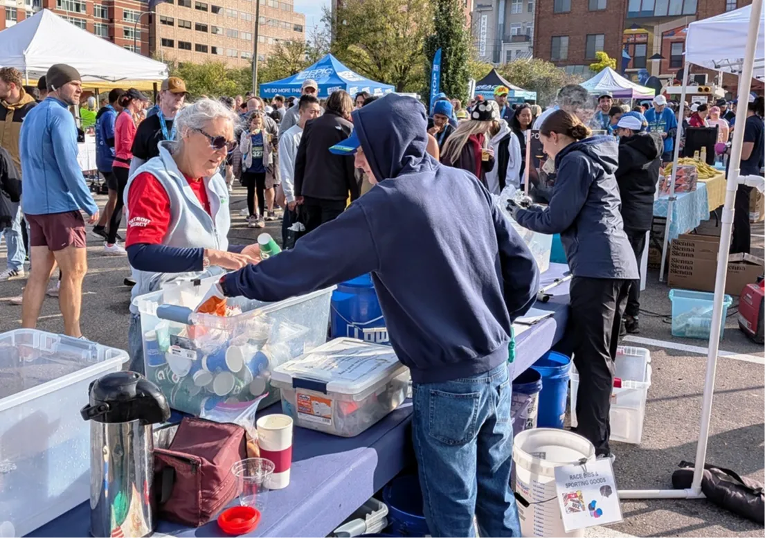 Volunteers handing out supplies to runners at a table before a race.
