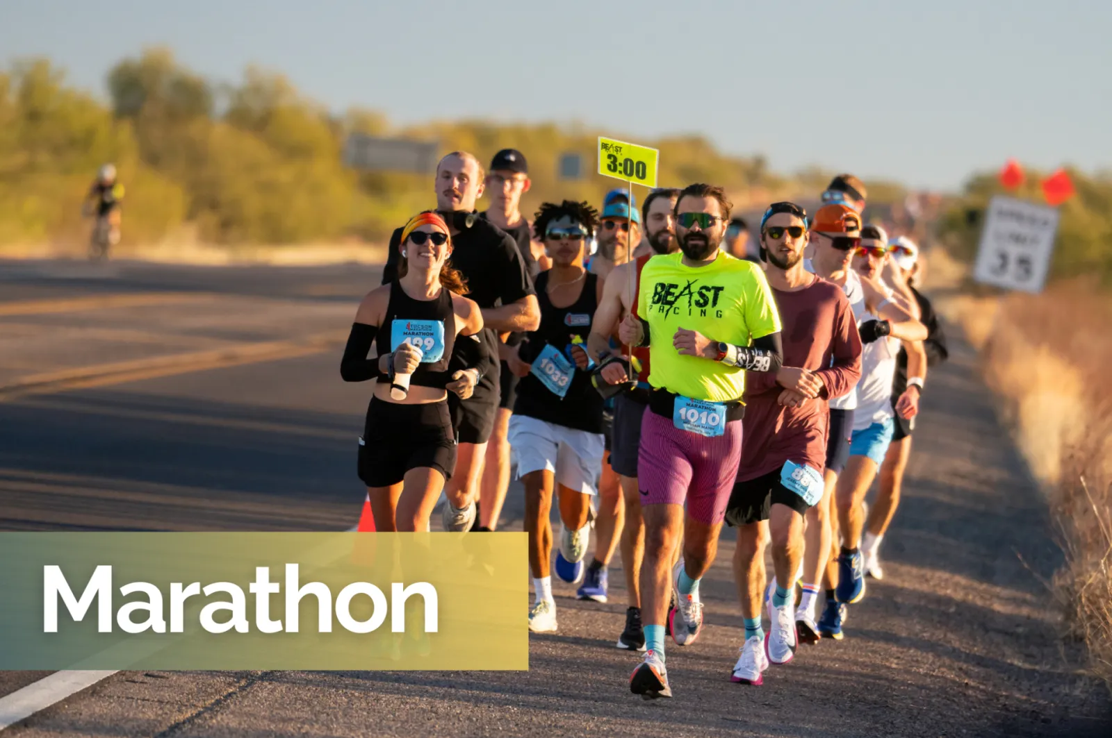 A group of runners participating in the Tucson Marathon, with the lead runners in focus on a road course under a clear sky.