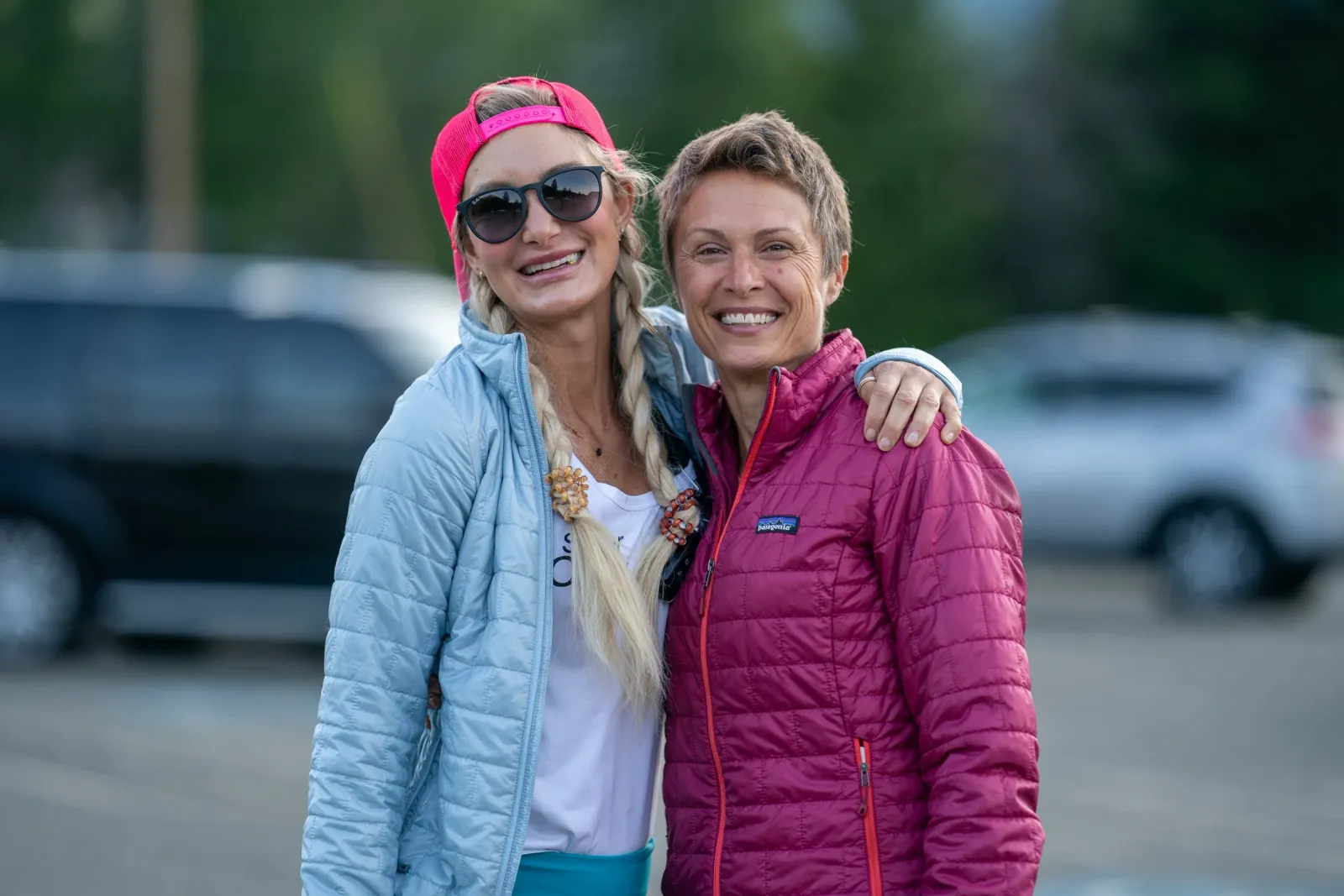 Two smiling women, one wearing a pink hat and sunglasses, pose for a photo.