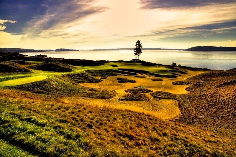 Scenic view of a golf course with rolling hills and a body of water in the background at sunset.